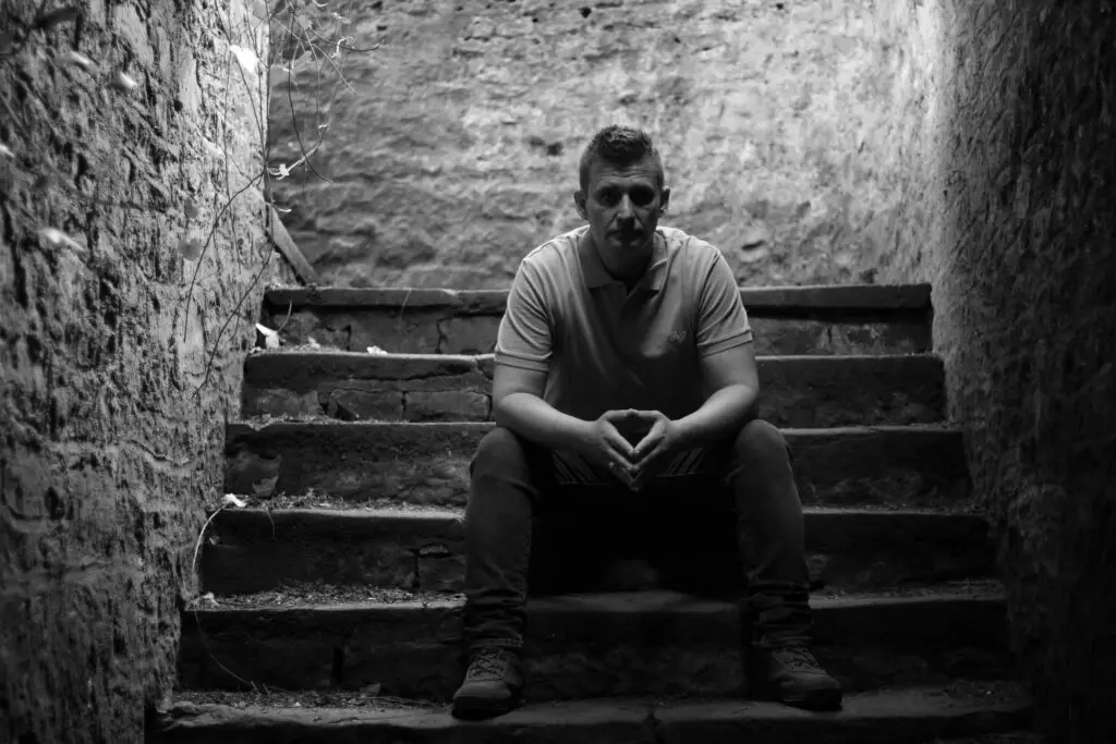 Black and white portrait photo of Ryan Kershaw sitting on stairs, looking seriously at the camera